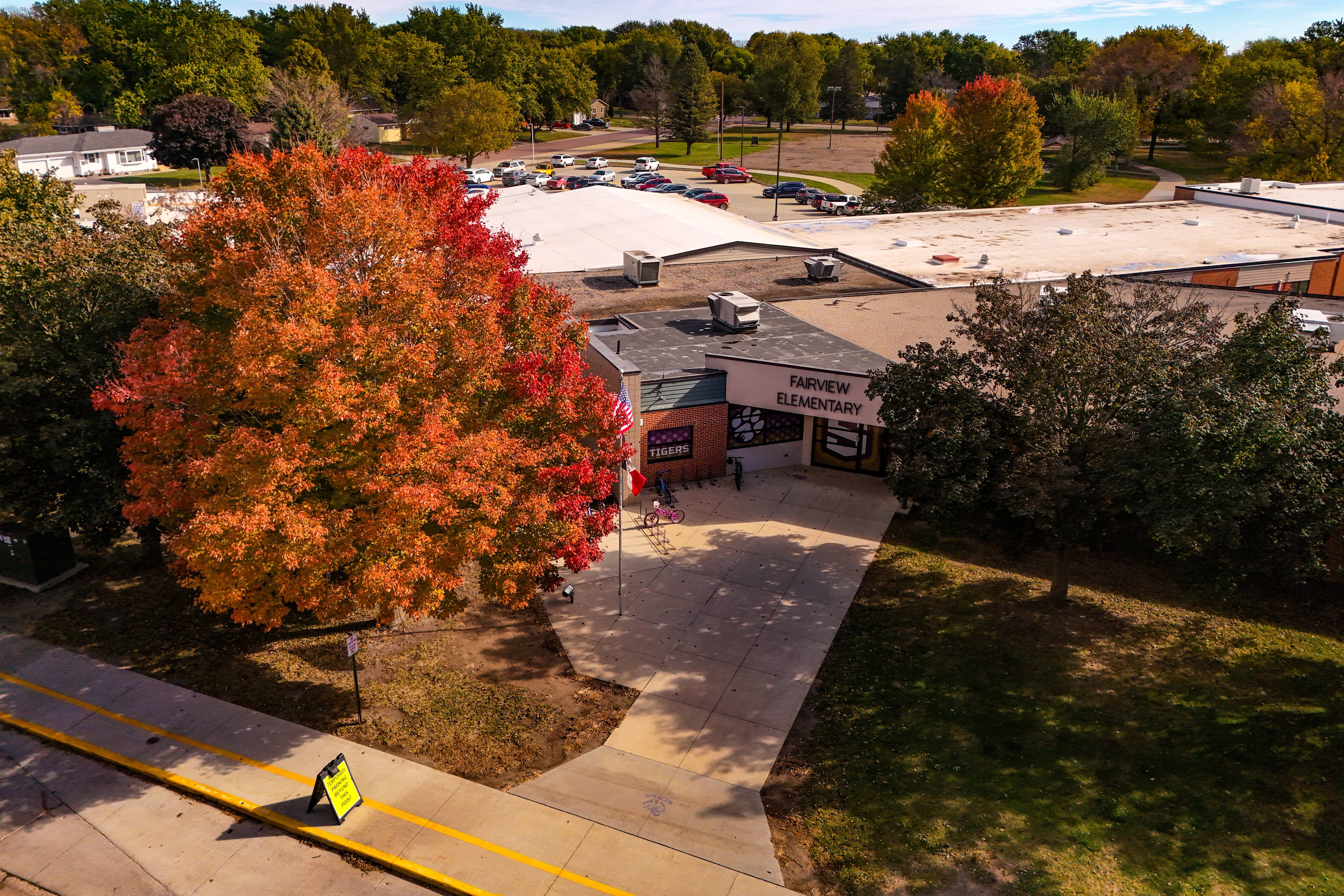 Aerial view of a commercial area with trees, a building, a driveway, and a large tree with autumn colors.