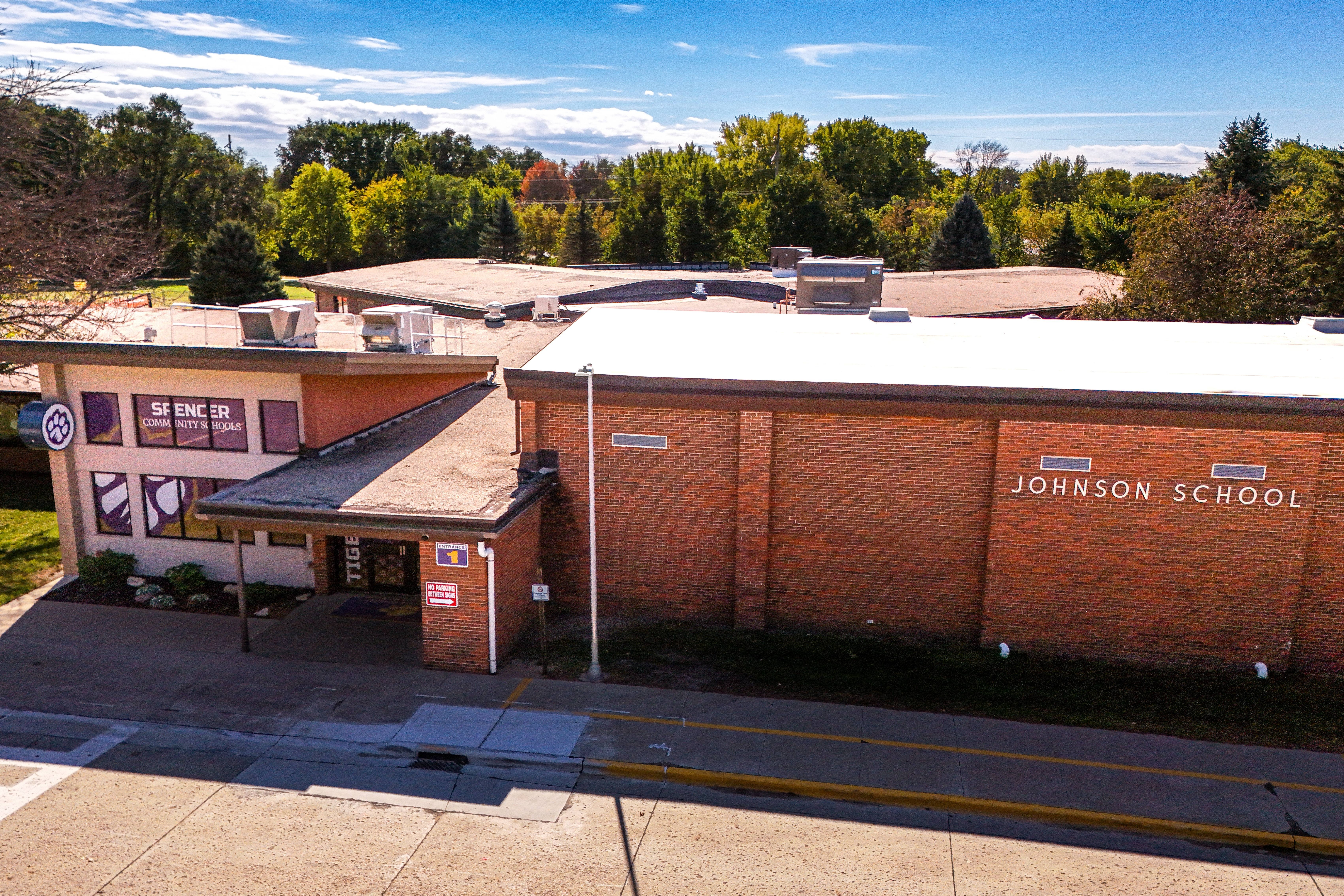 A building with a white roof and brick walls. The words "Jefferson School" are on the side. Trees and a blue sky are in the background.