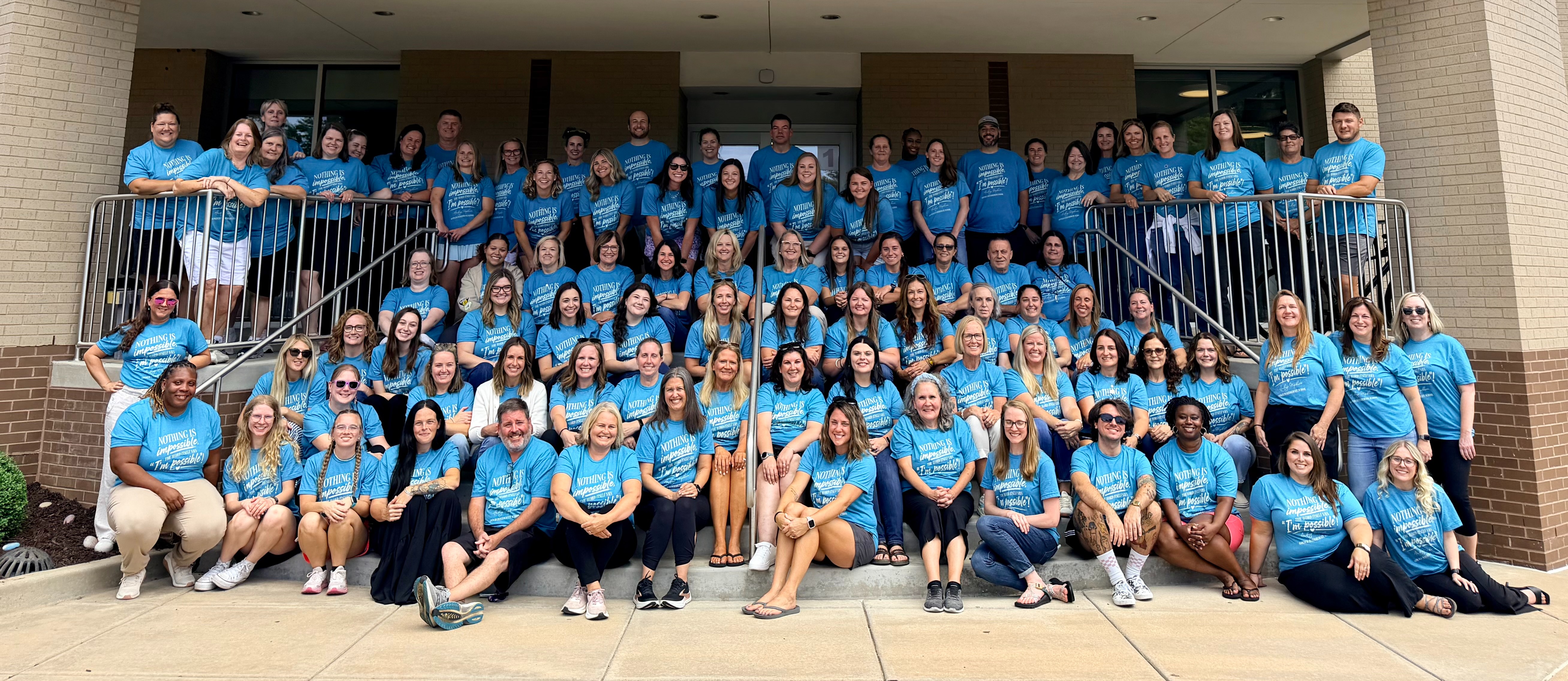 Photo of Gotsch staff sitting on front stairs of school wearing matching shirts.