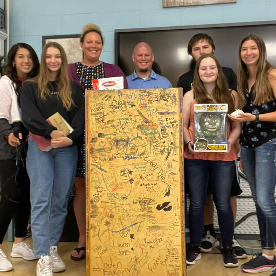 Teachers and students pose around a signed podium with gifts