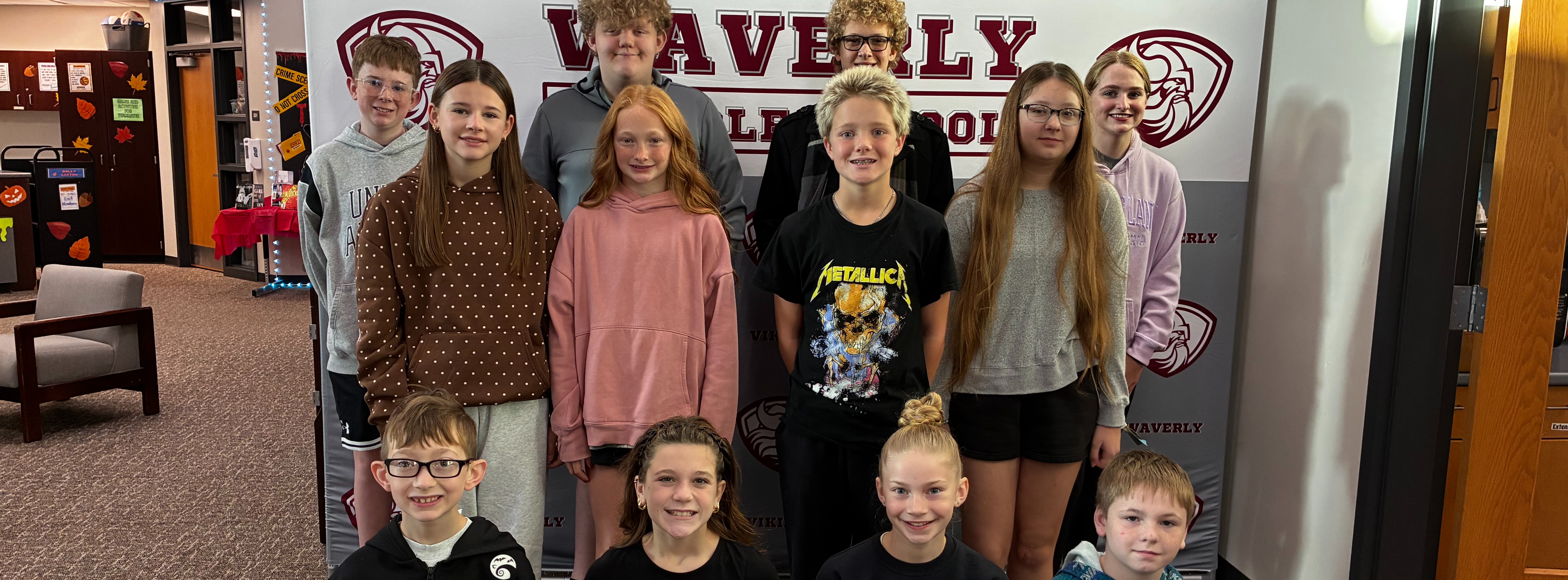 A group of children and adults stand in front of a banner displaying "Waverly" and a logo.