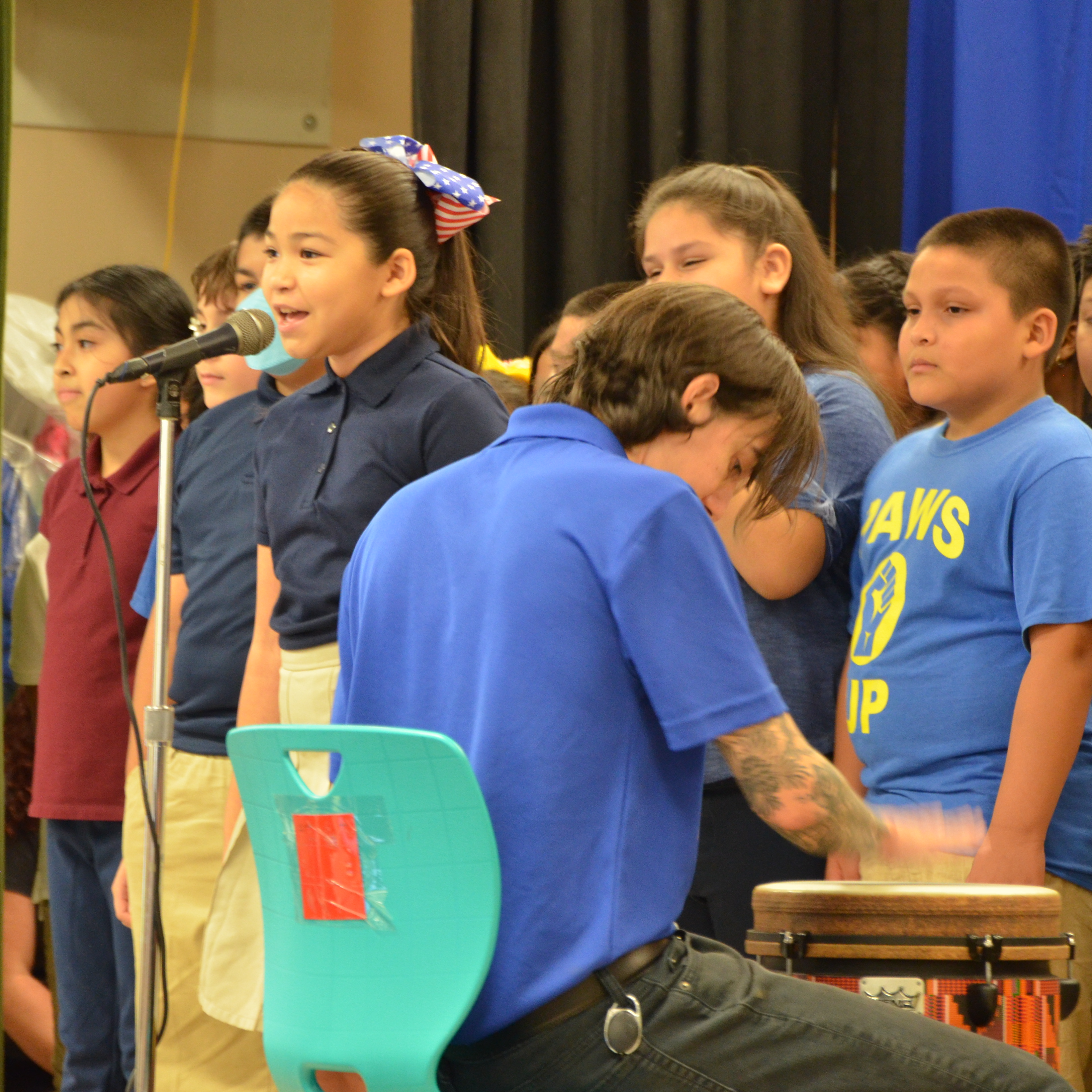 Students singing on stage with their music teacher during a governing board meeting