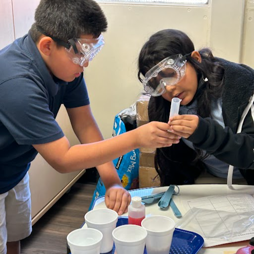 two students conducting a science project wearing googles and holding a tube together 