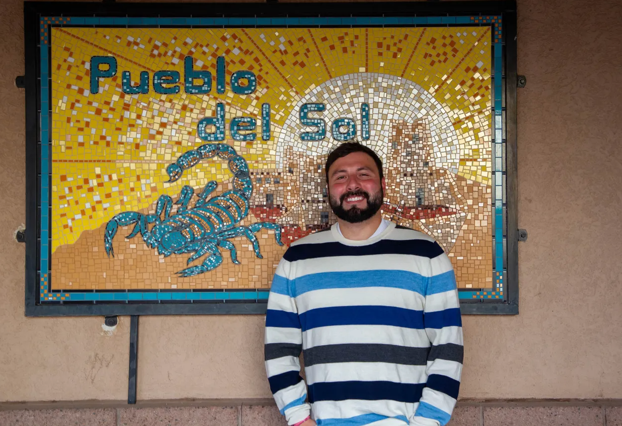 Pueblo Del Sol teacher standing in front of a PDS tile mural