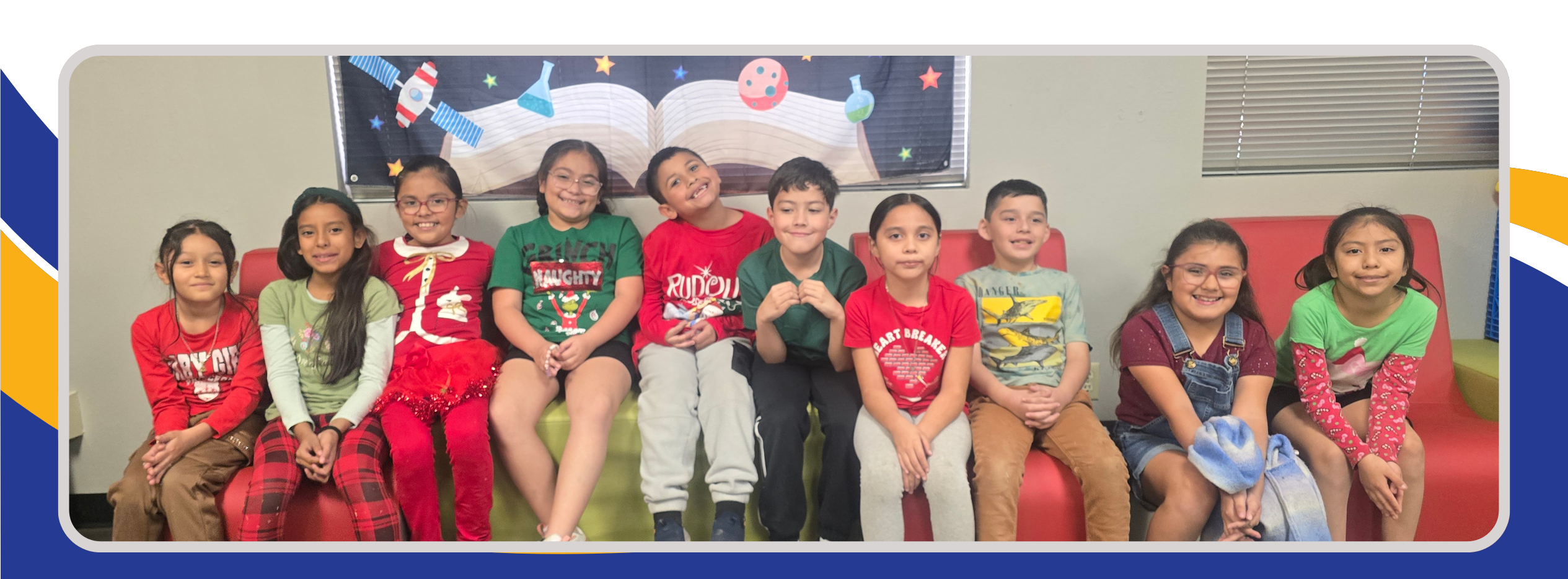 A group of 3rd grade students sitting on couches, wearing festive green and red attire as part of our school's Holiday Spirit Week. The students are smiling and posing together, showing off their holiday-themed outfits.