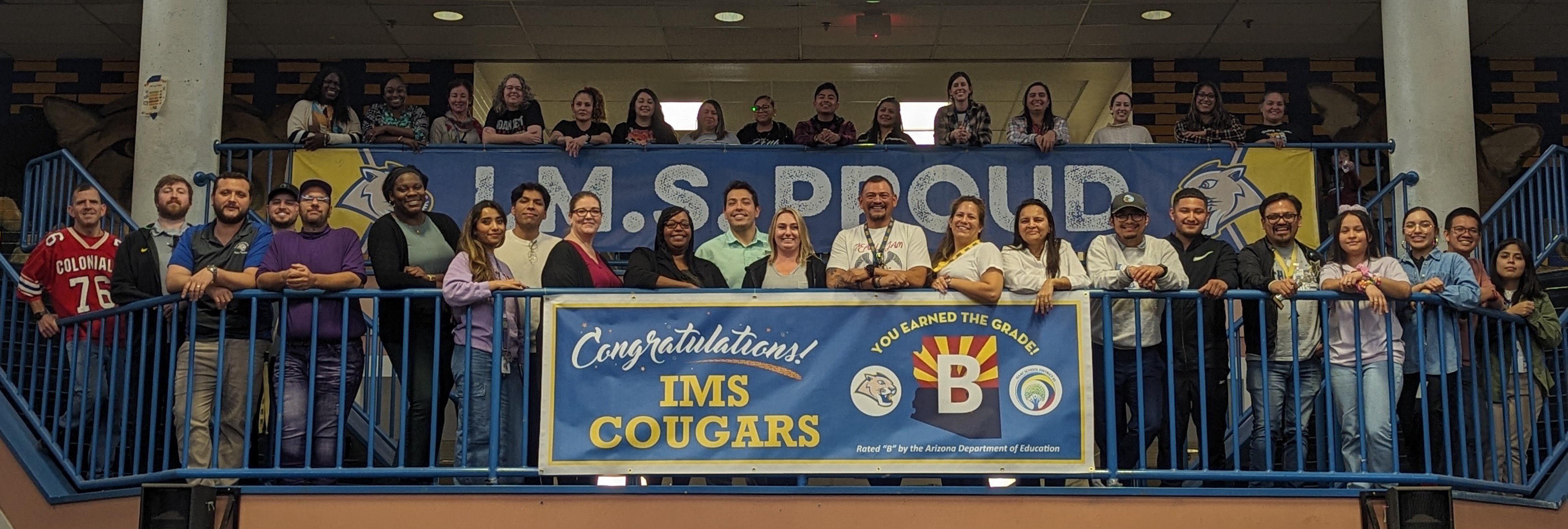 Large group photo of the IMS staff standing in front of sign that says congratulations IMS Cougars! You earned the grade. Rated "B" by the Arizona Department of Education 