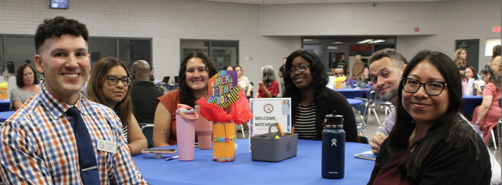 Principal sitting at a round table with new teachers; they all appear to be happy;  New Staff Orientation