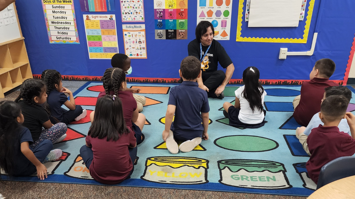 Elementary students sitting on the carpet with their teacher while they learn about the different letters of the alphabet.