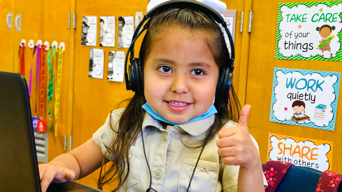 Kindergarten student giving a thumbs up while working on her student chromebook in the classroom.