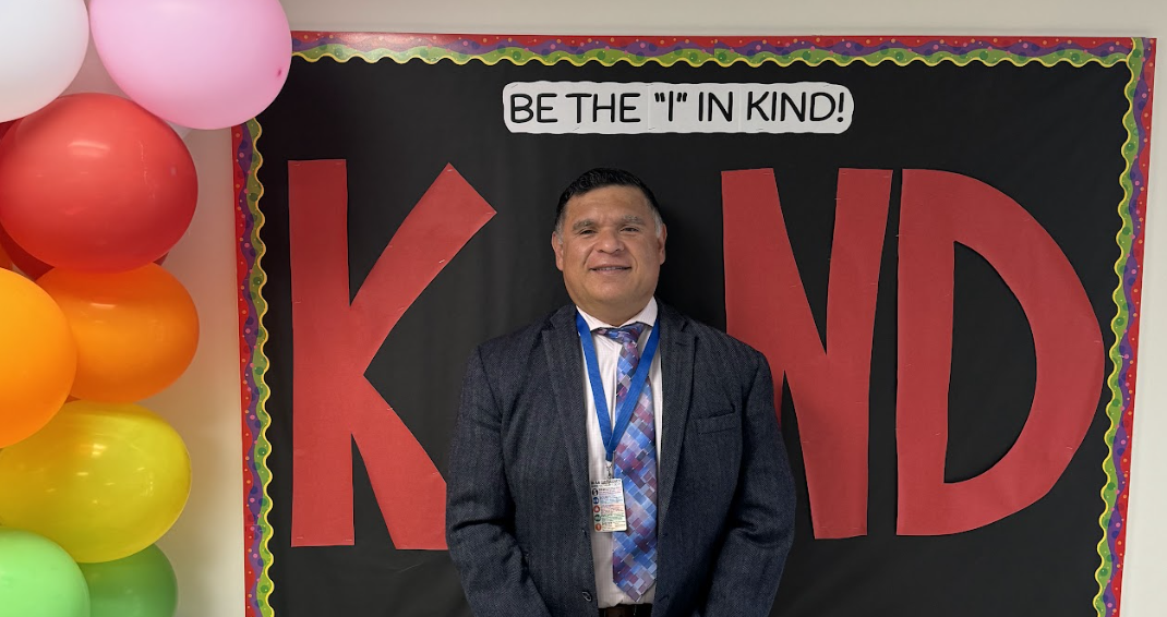 Superintendent Rene Sanchez posing in front of a school's  "Be the "I" in Kind" bulletin board.