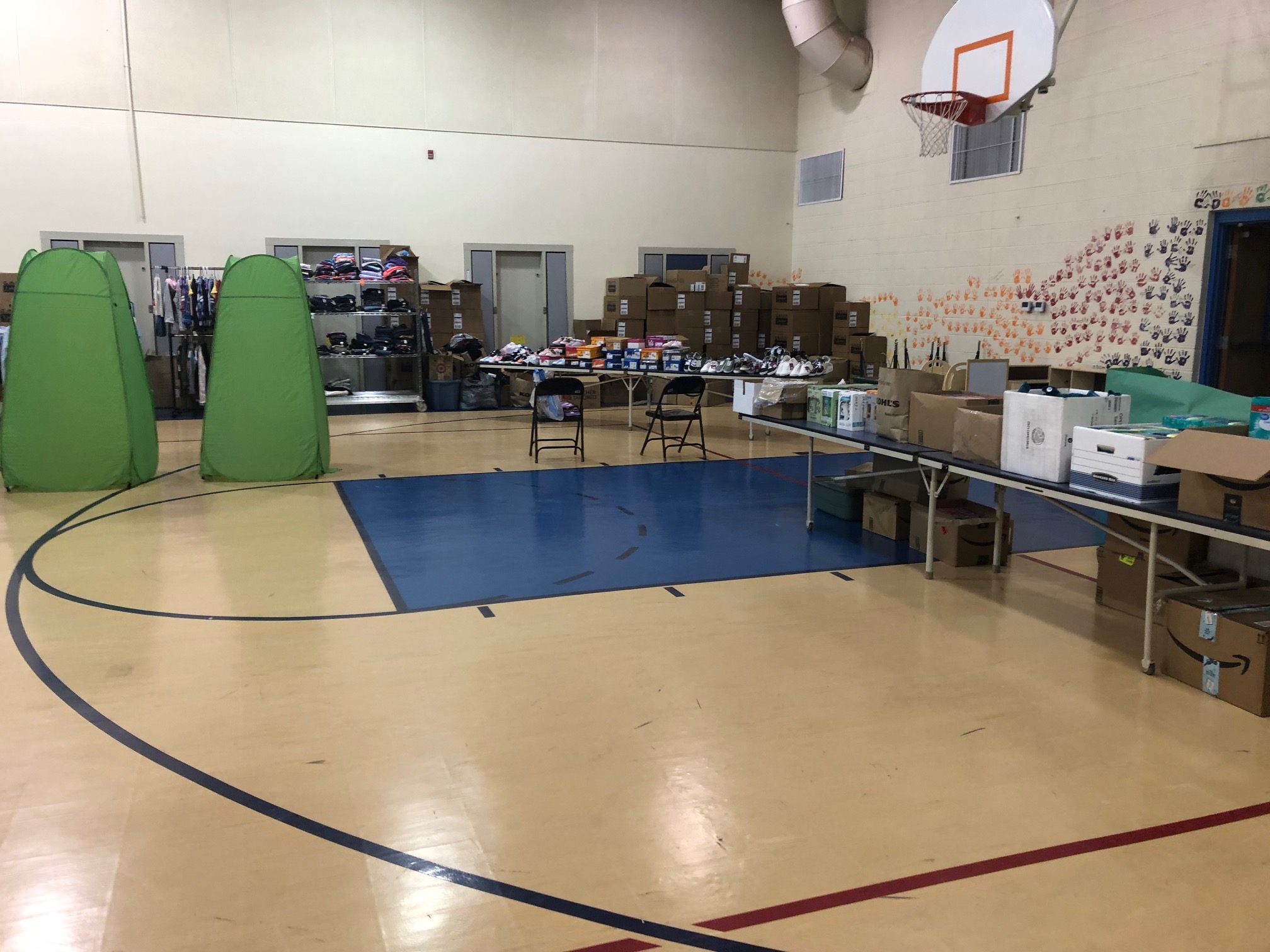 Tables, racks, and fitting room tents set up in a gymnasium for students to pick out clothes, shoes, and other school supplies.