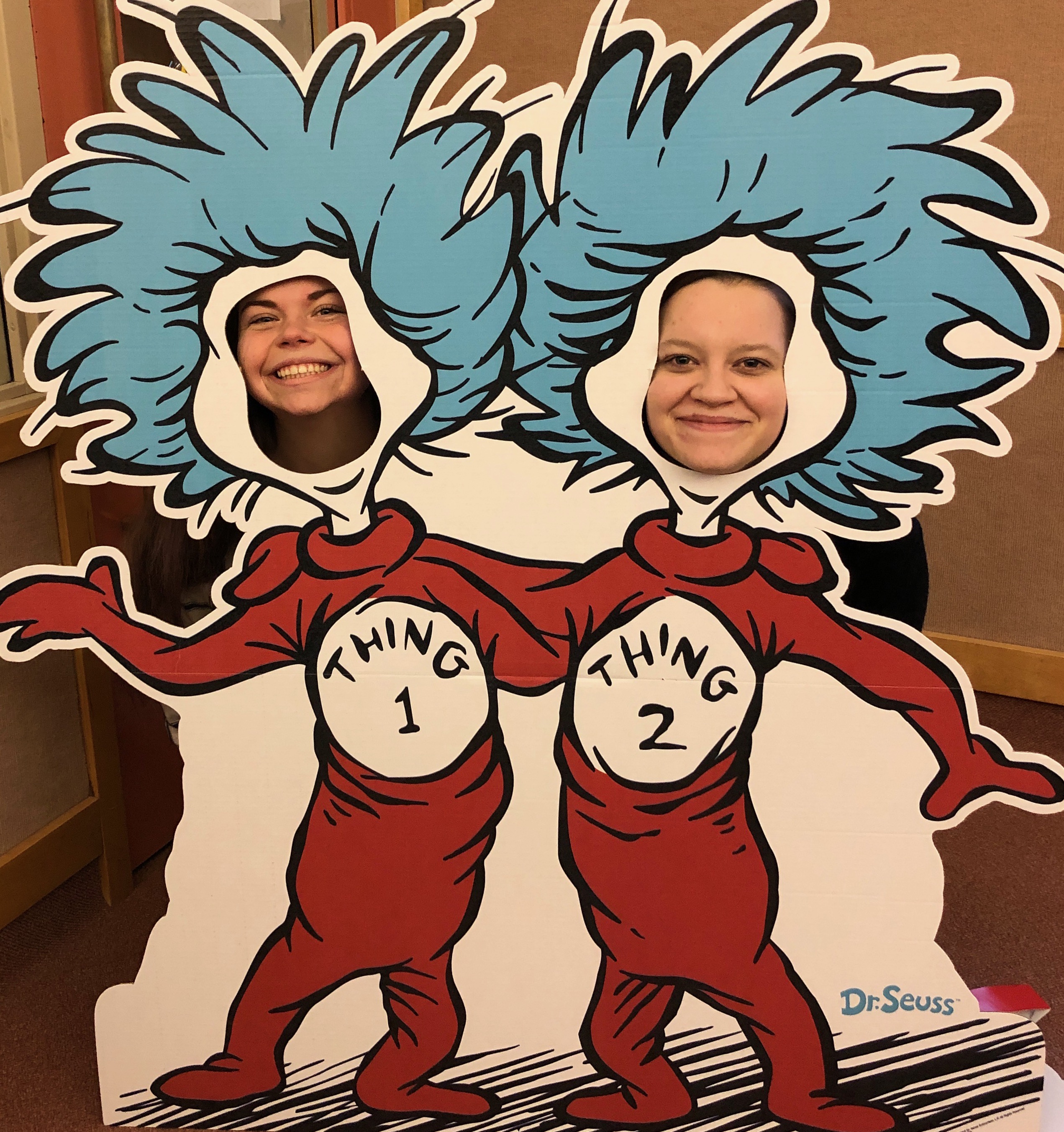 Two girls stick their heads through face cut-outs, their bodies are thing 1 and thing 2