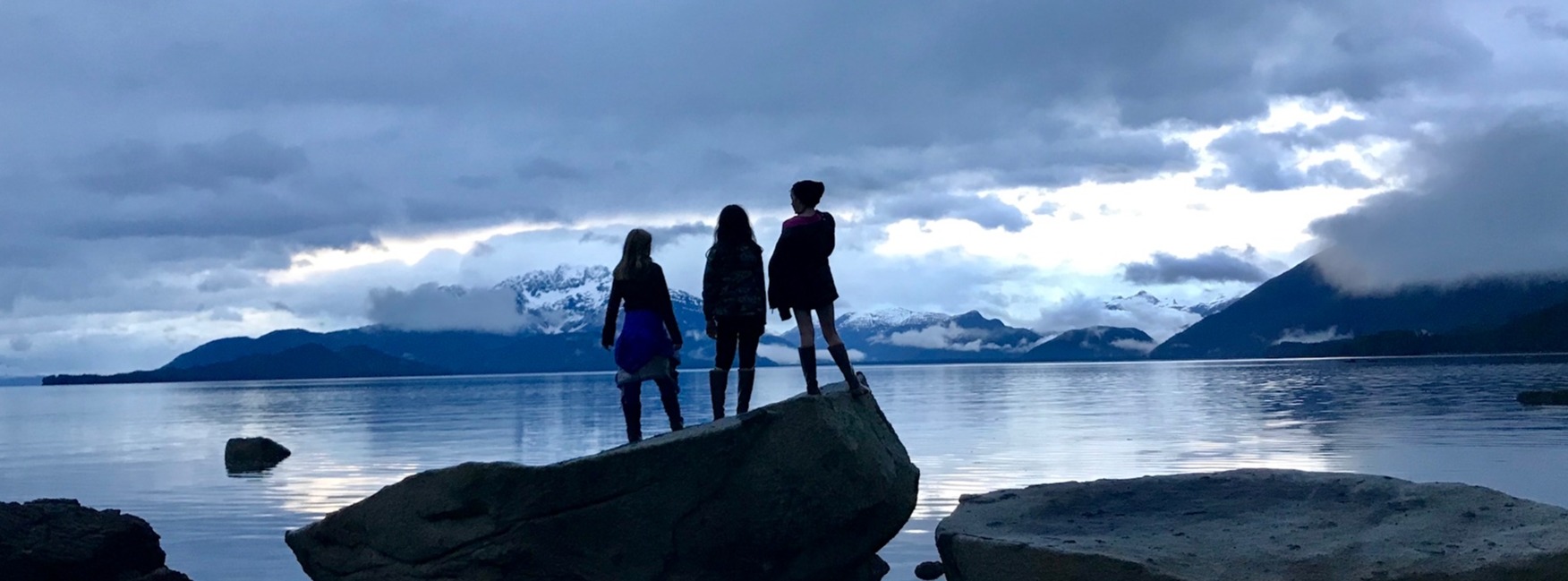 Three students standing on a rock by the ocean