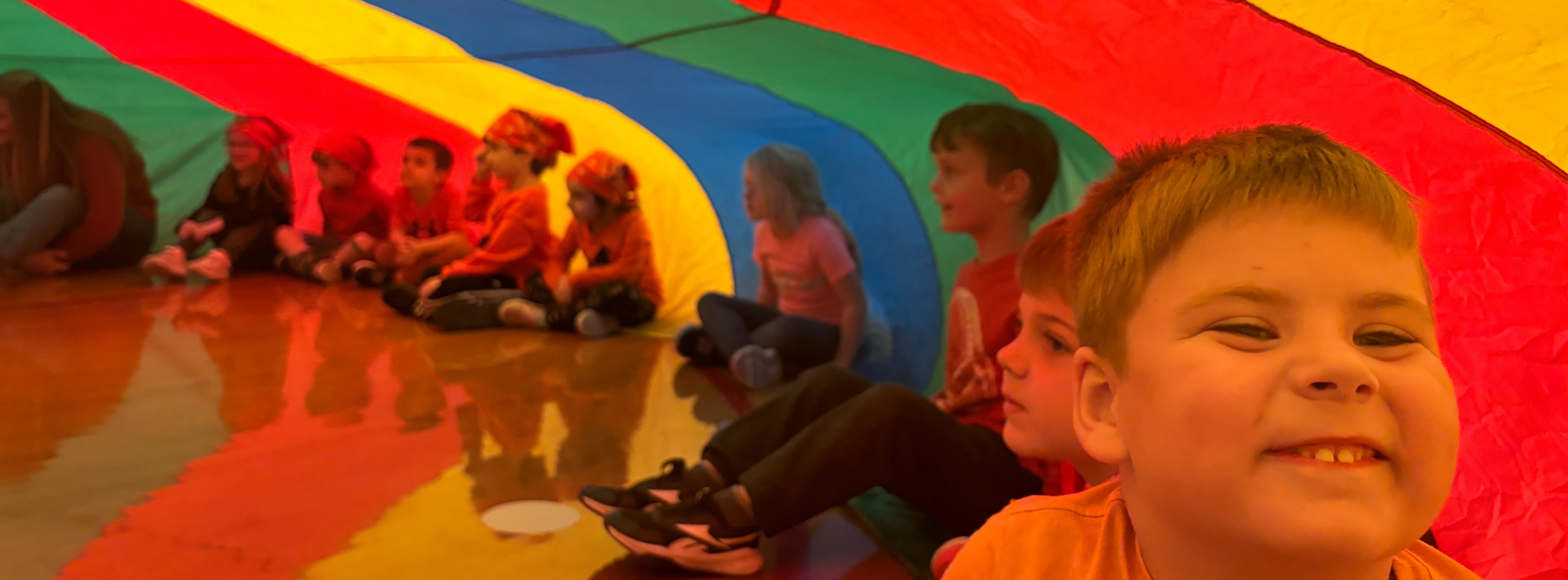 kindergarten students inside giant rainbow colored parachute