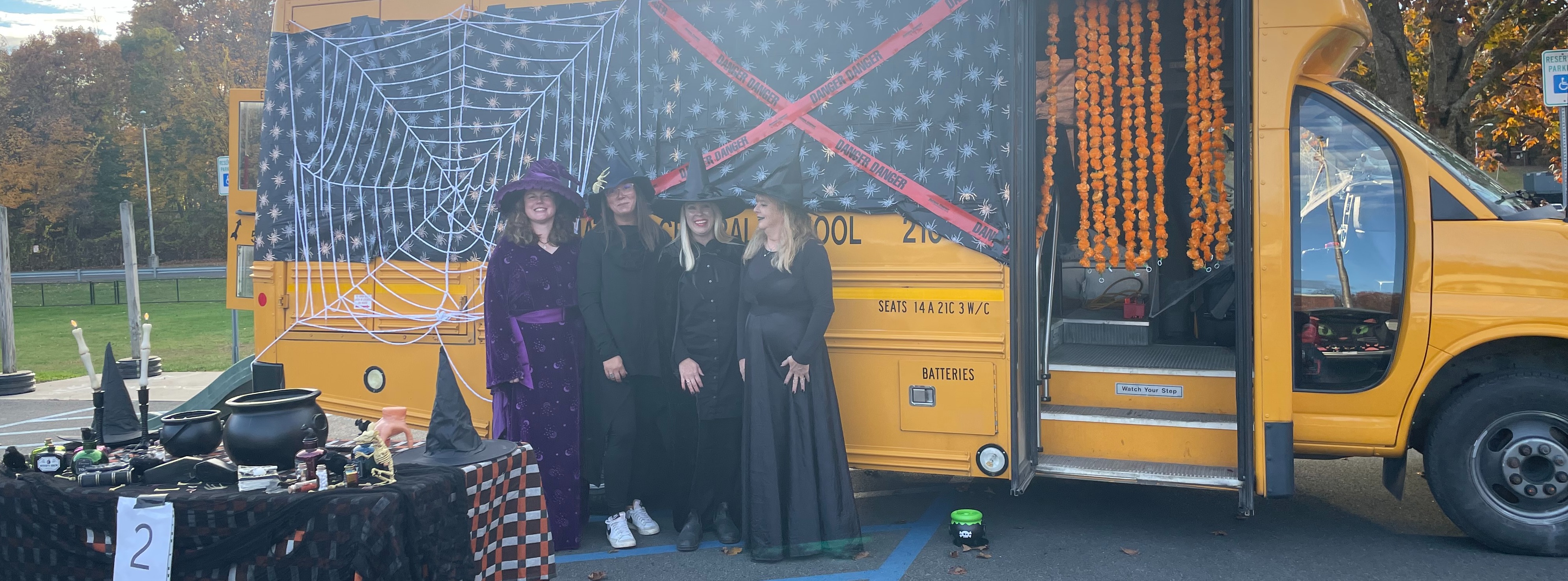 women dressed as witches standing in front of school bus that has been decorated for Halloween