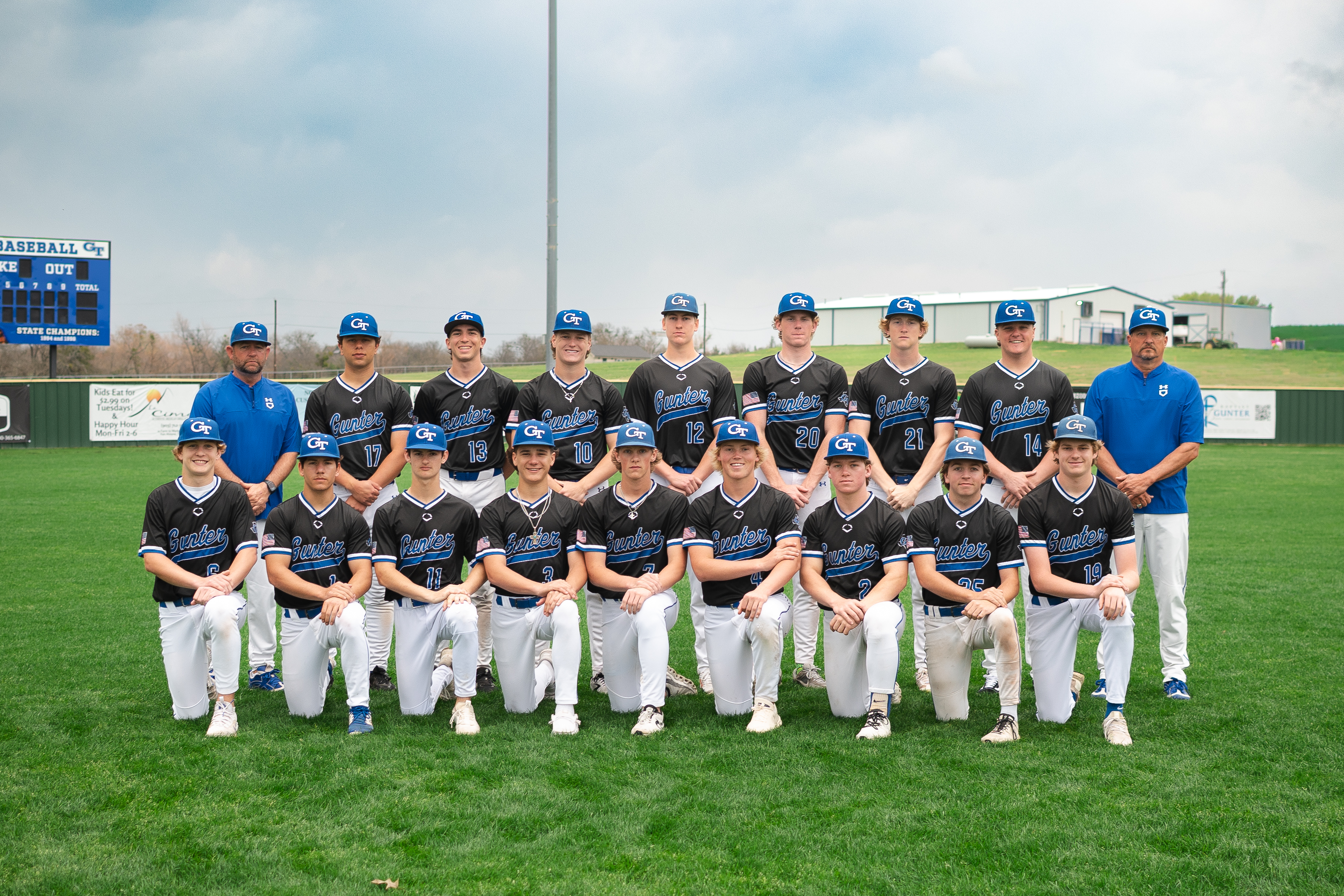 A baseball team wearing blue and white uniforms and hats, posing for a photo on a field.