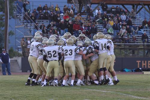 A photo of the football team in a huddle on the football field at a game