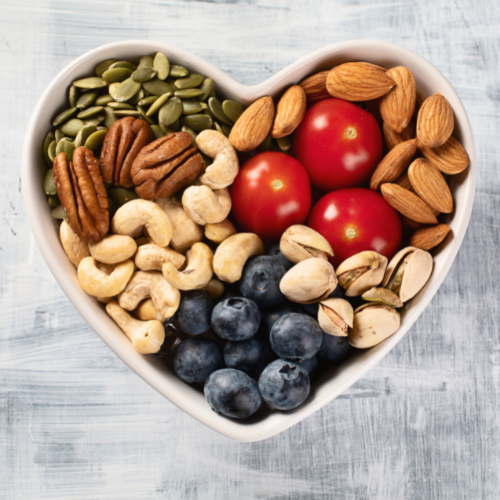 Nuts, seeds, blueberries, and cherry tomatoes in a white heart-shaped bowl.