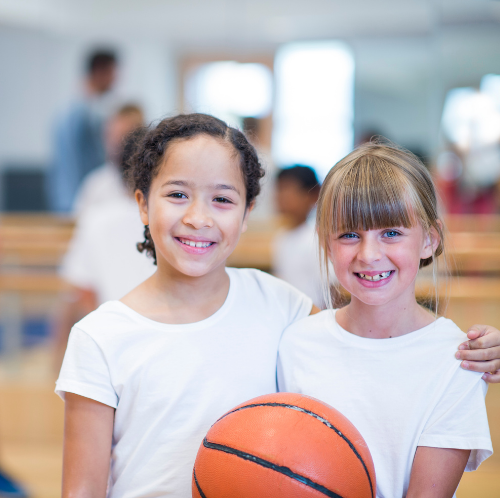 Two girls smiling; one is holding a basketball.