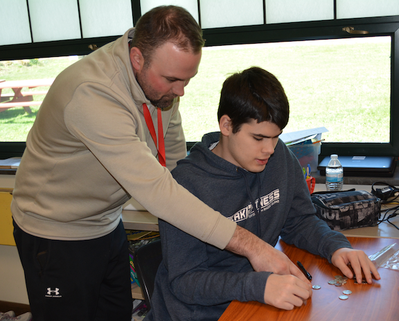 Teacher assisting student counting money.