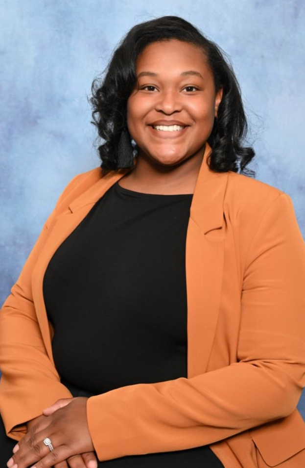 A woman in an orange jacket and black shirt is smiling.