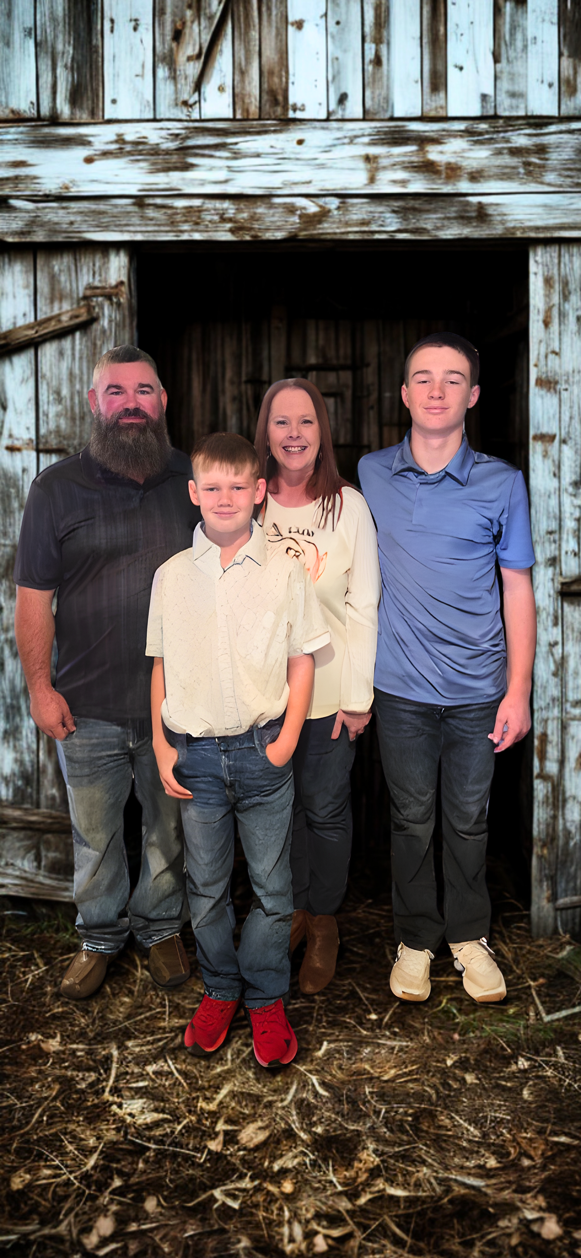 Four people pose for a picture in front of a barn. A man, a woman, and two boys.
