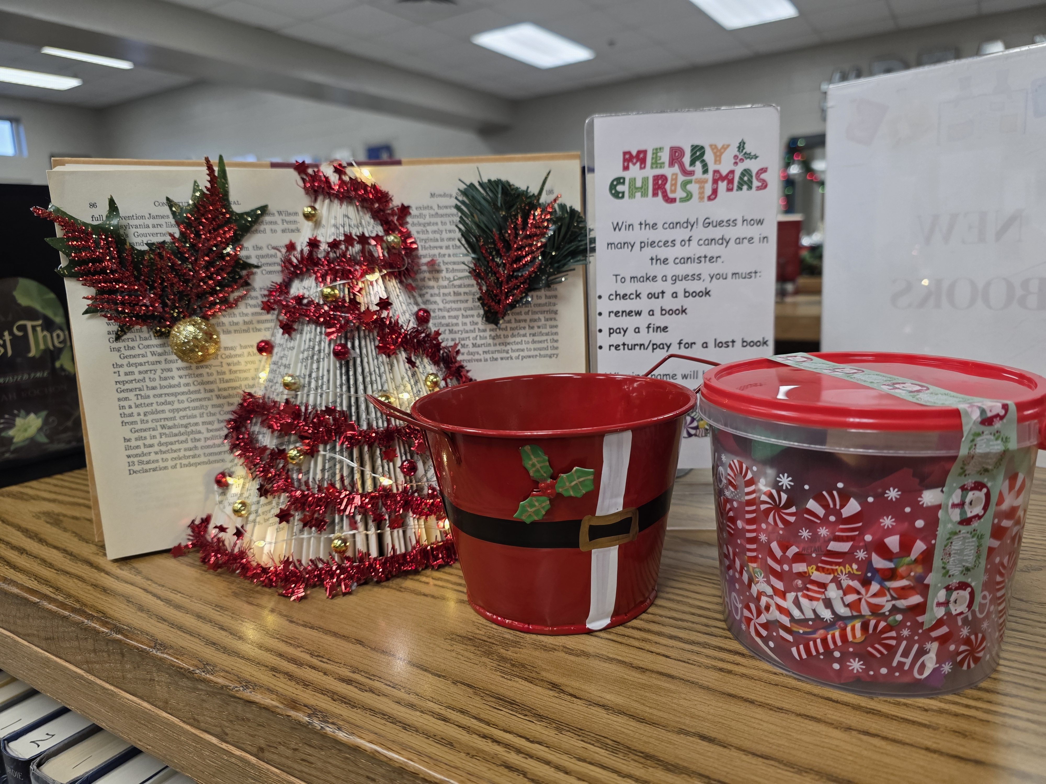 Christmas tree made out of a book next to a jar of candy with a sign telling patrons to guess how much candy is in the jar