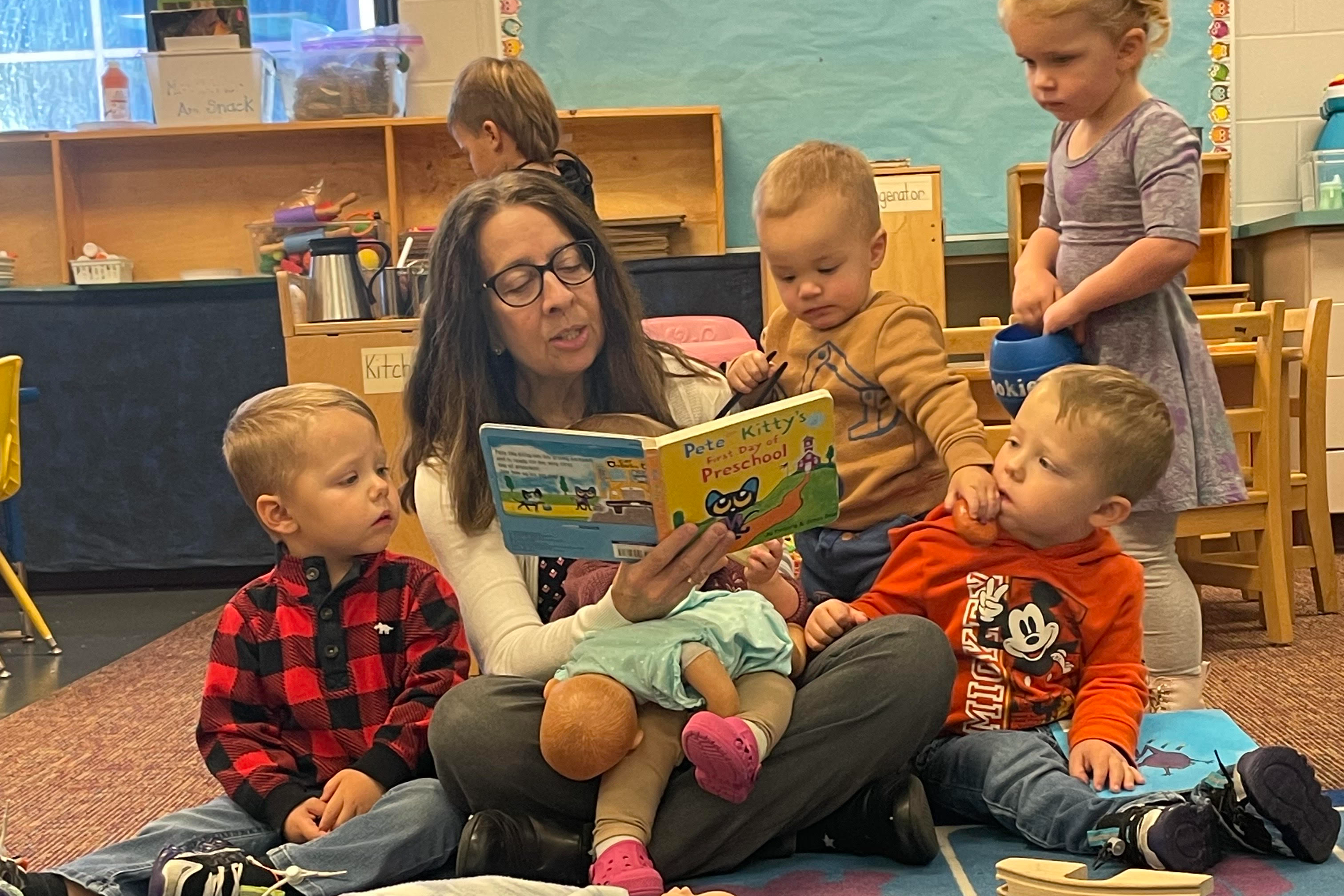 Children sitting with their teacher reading a book 