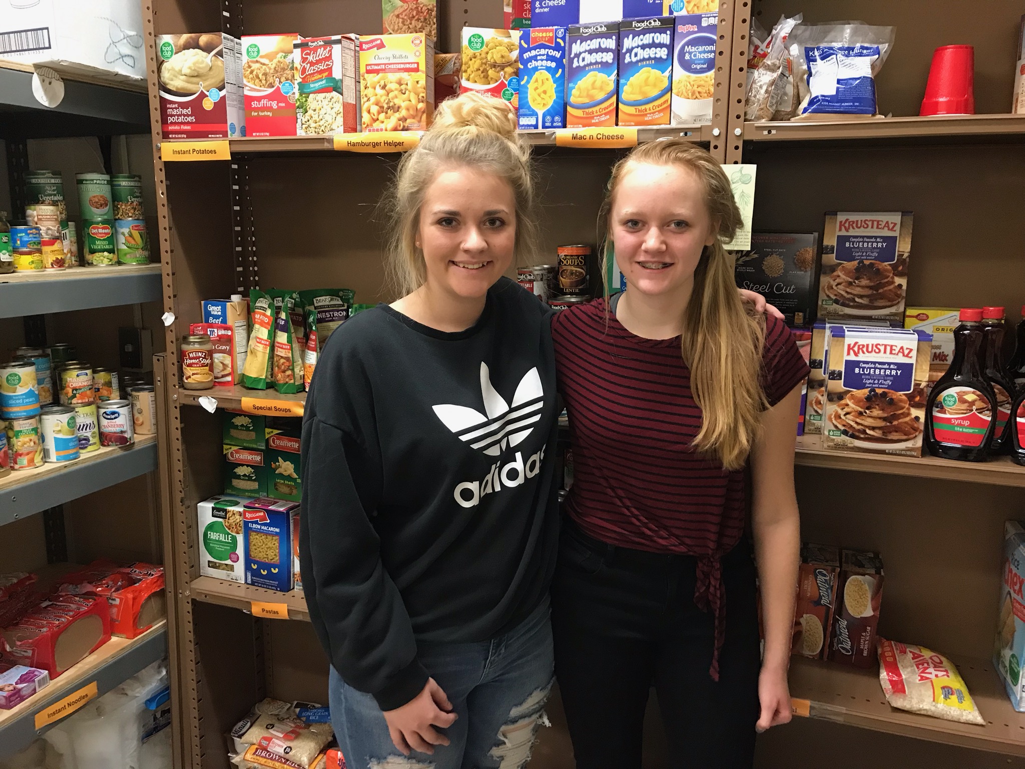 Two student helpers standing in front of shelves with food on them