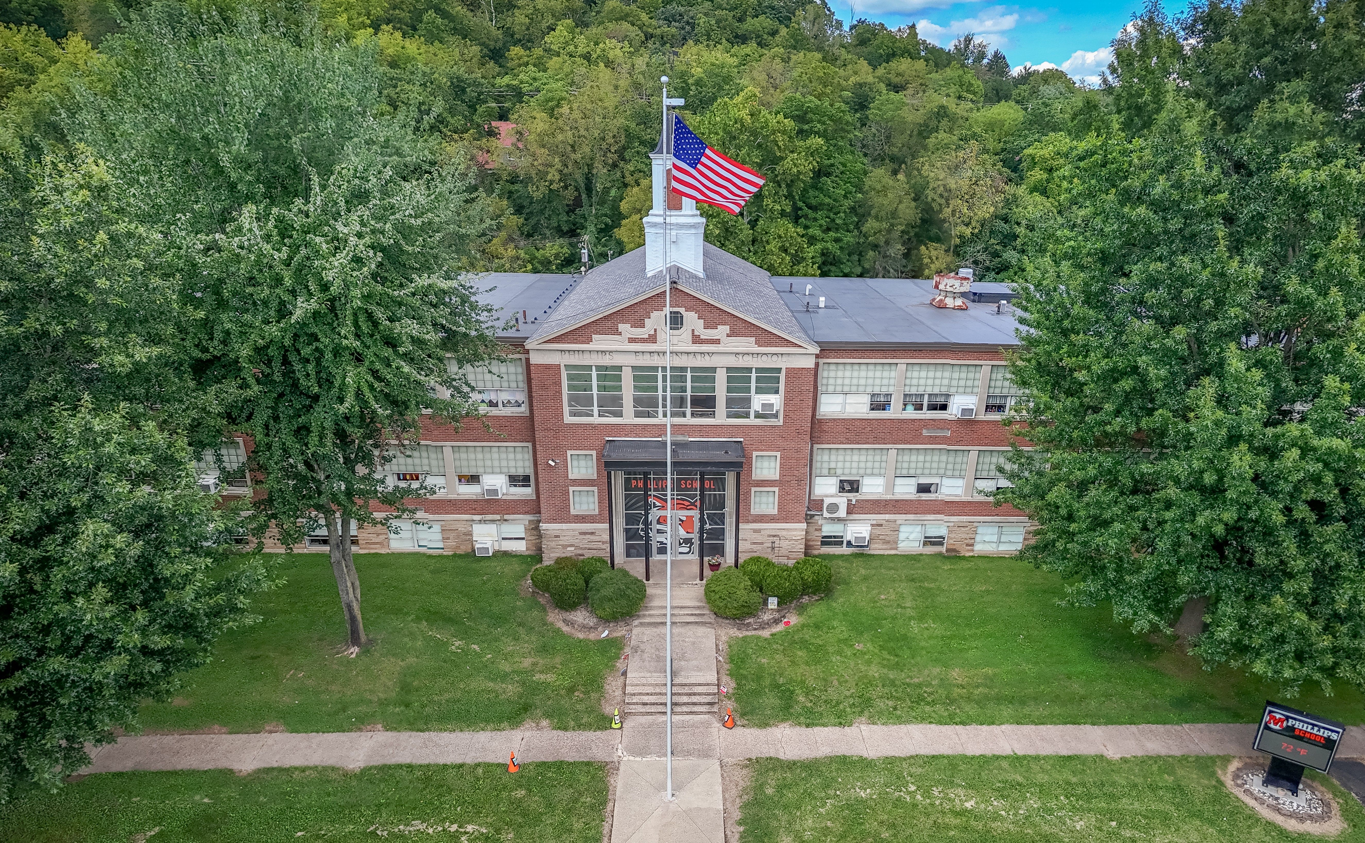 Aerial view of a school building with flag, trees, and lawn. Front entrance with walkway.