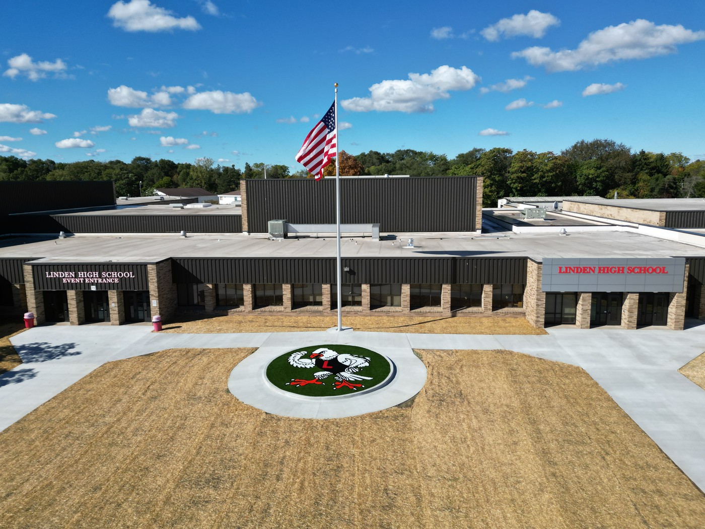 Drone shot of exterior of high school building with tuffy mascot painted on a turf circle with flag pole and american flag