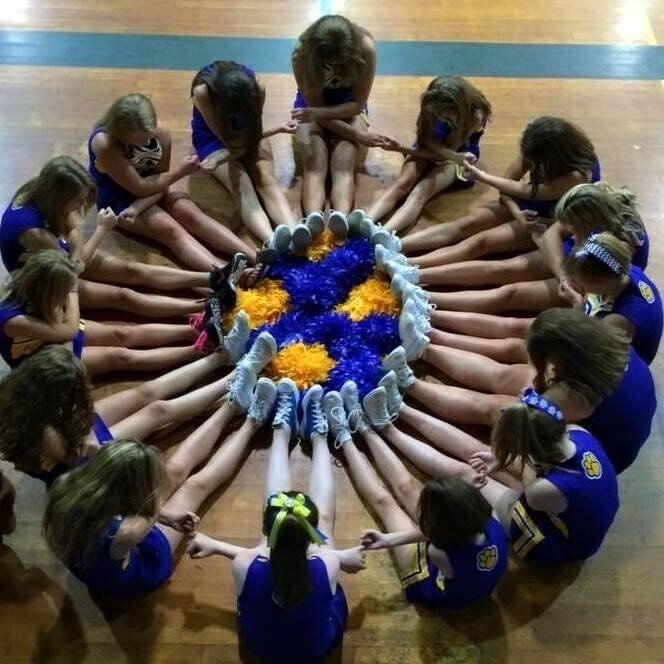 Cheerleaders sitting in a circle will pom poms in the middle