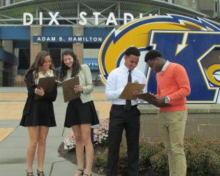 four students work on documents outside of Dix Stadium