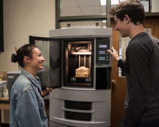 Two students work with large 3-D printer