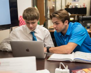 two boys in dress clothes collaborate on laptop