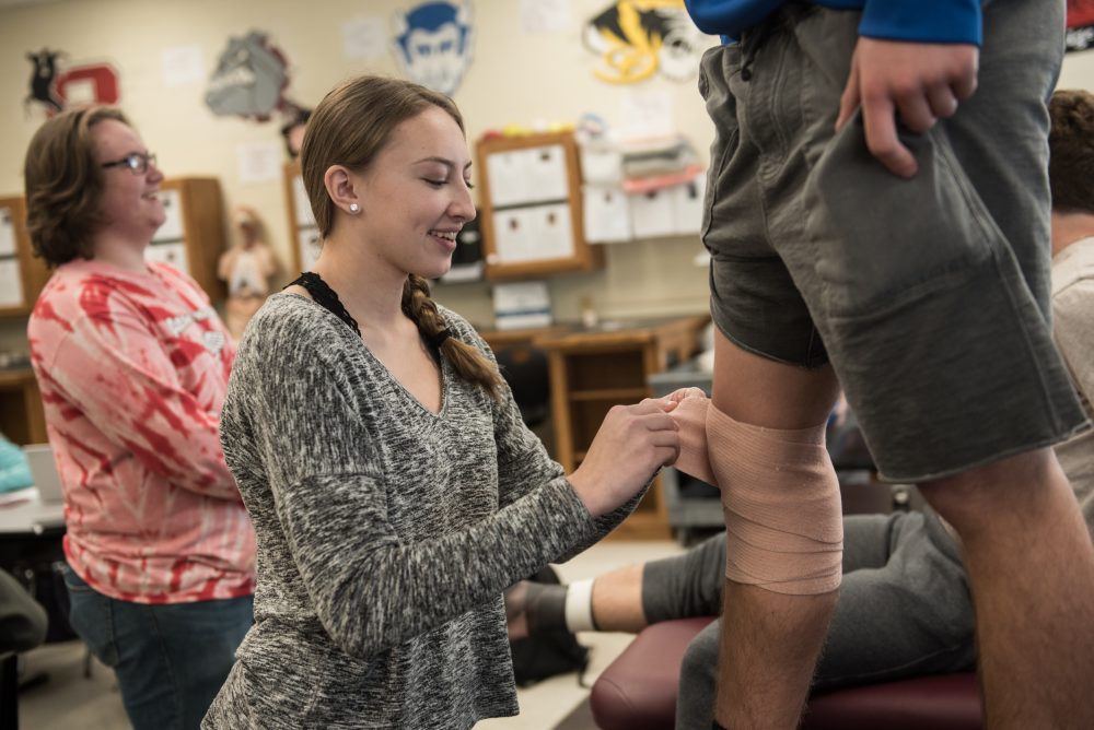 A student practing wrapping a knee in bandages