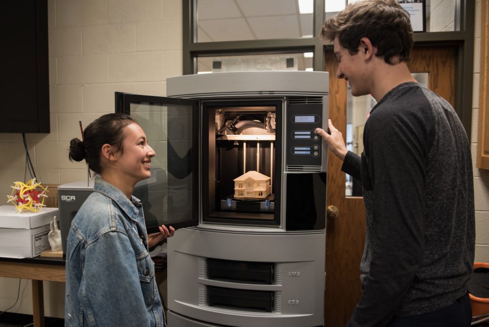 2 students standing next to a 3D printer