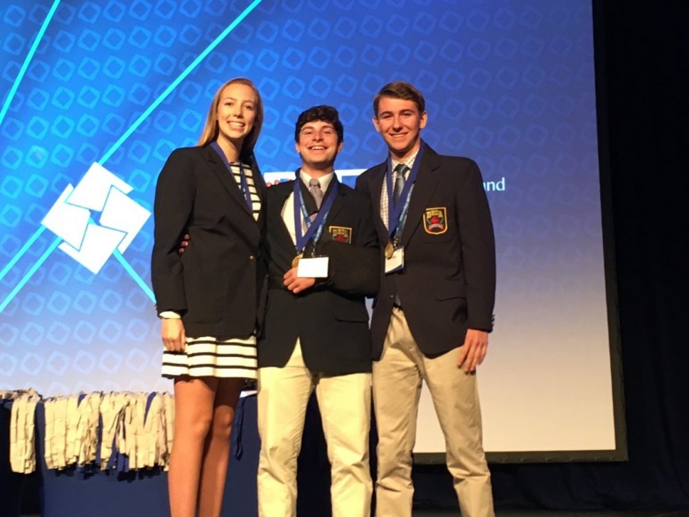 3 DECA students with medals on stage