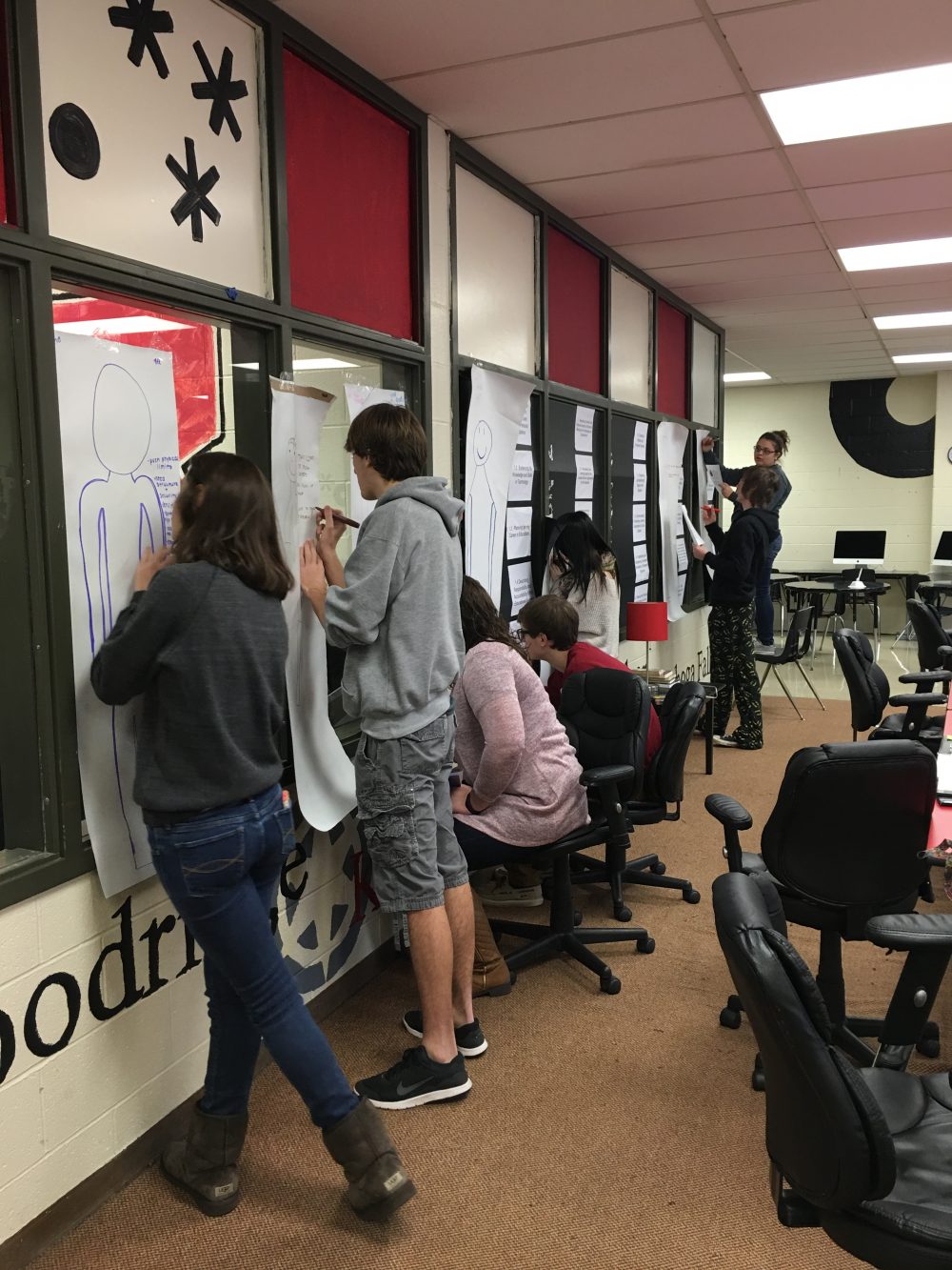 Students writing on paper that's attached to the wall