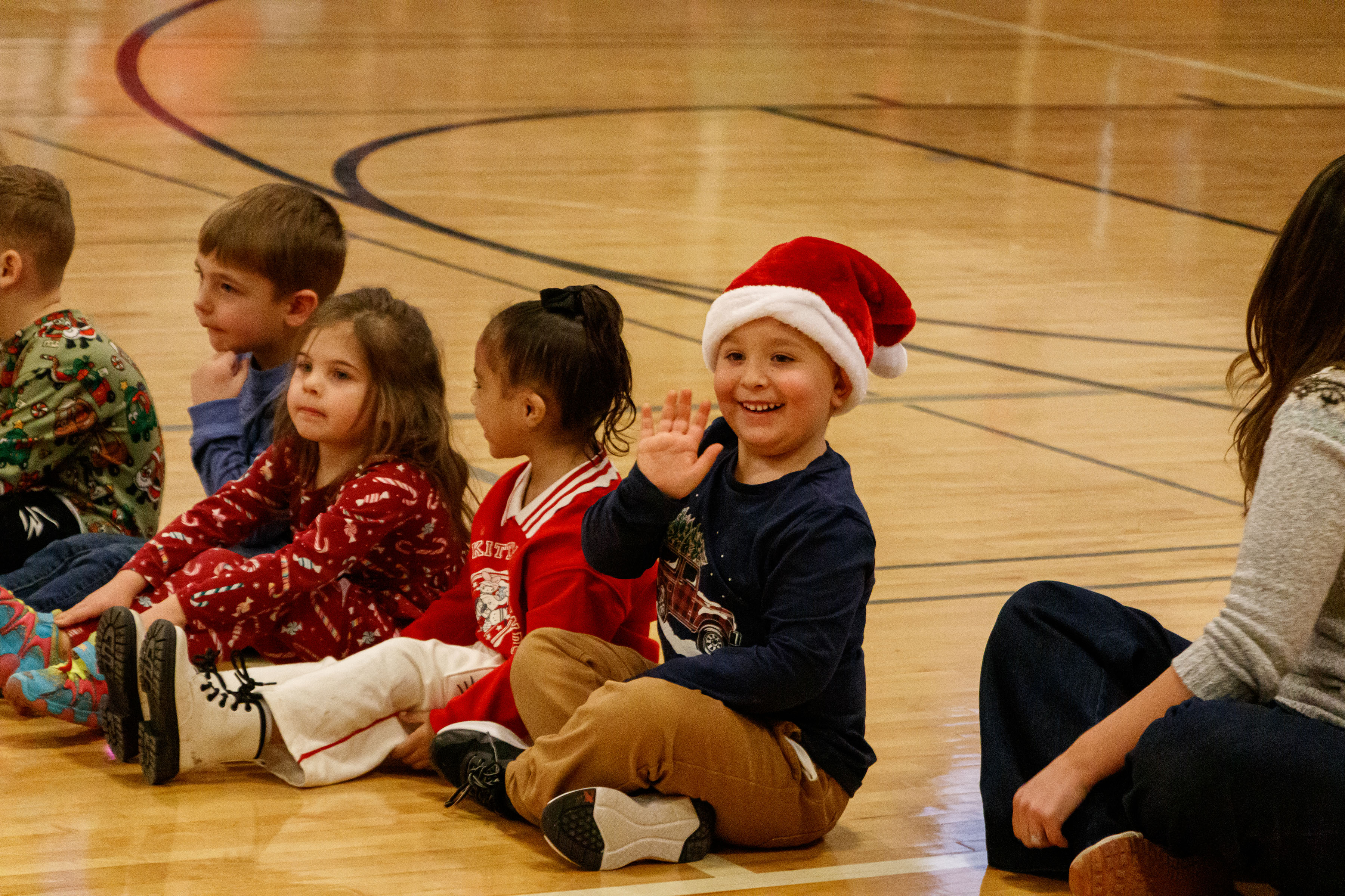 Student in Santa hat waves at the Elementary Sing Along