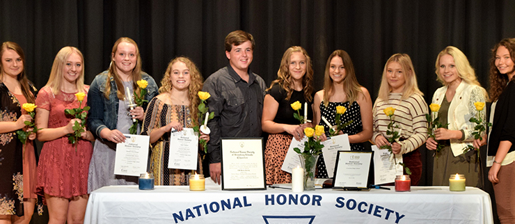 National honor society group photo with all students gathered around table holding flowers and rewards 
