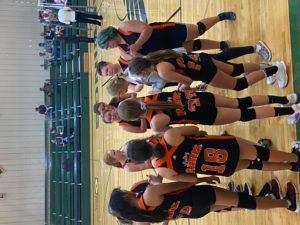 junior high volleyball players in huddles with coaches during game in gym. CPS players in black & orange uniforms