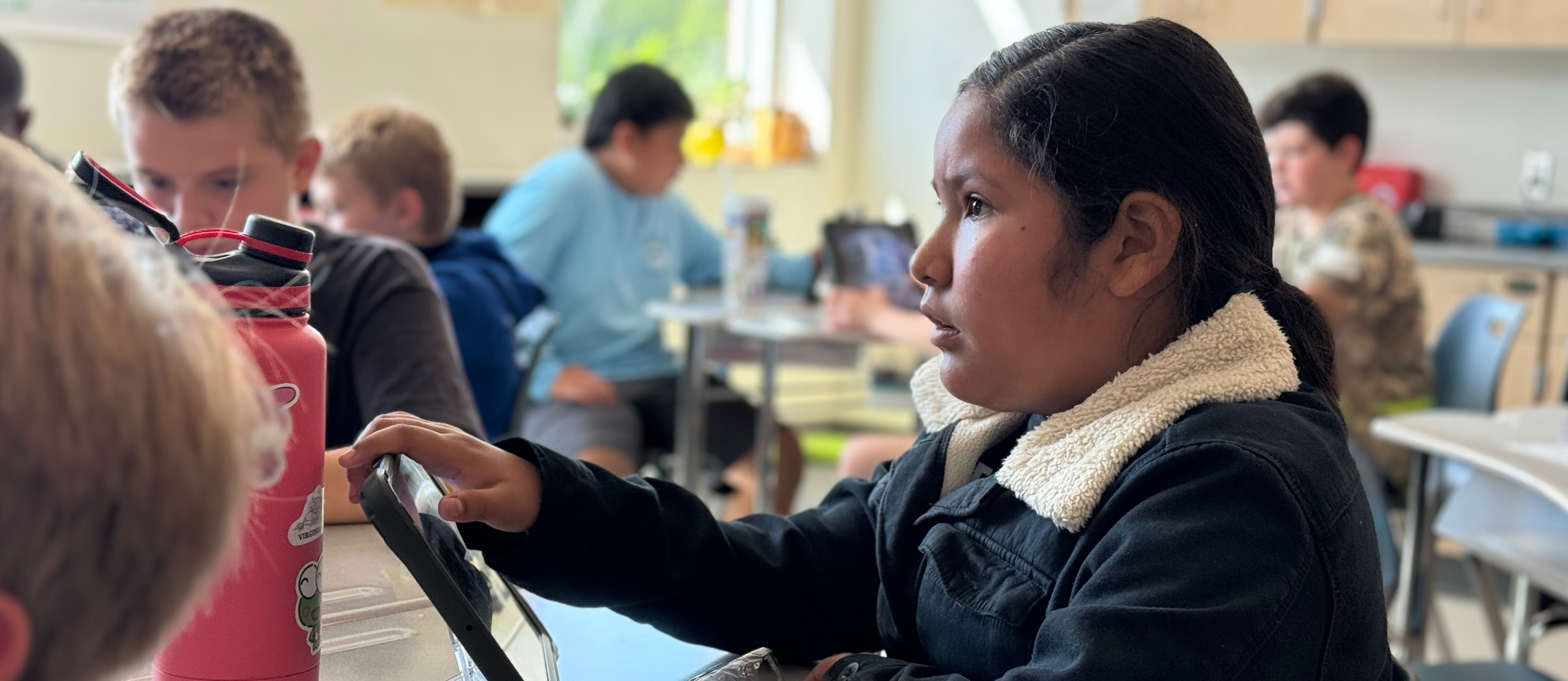 Student using an iPad looking to the front of the room 