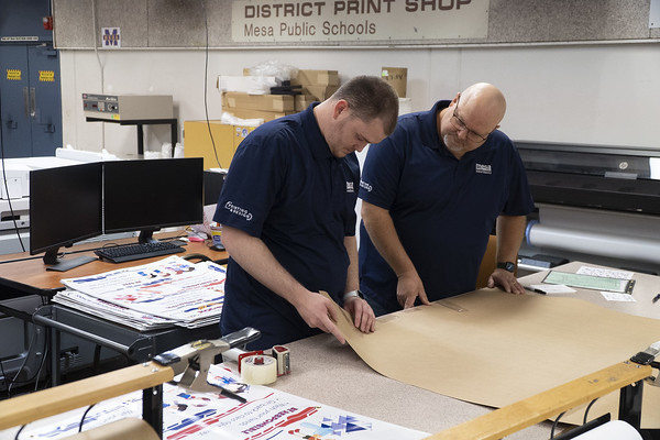 two print shop employees looking standing at a table looking at a print