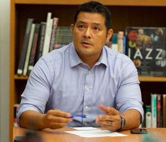 committe member sitting at a table with paper and cell phone on the table and pen in his hand