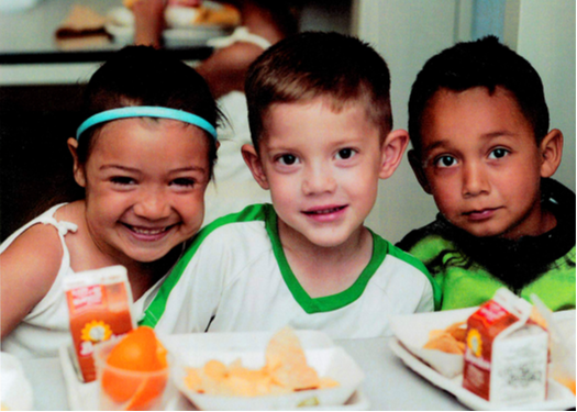 three children smiling while eating their lunch 