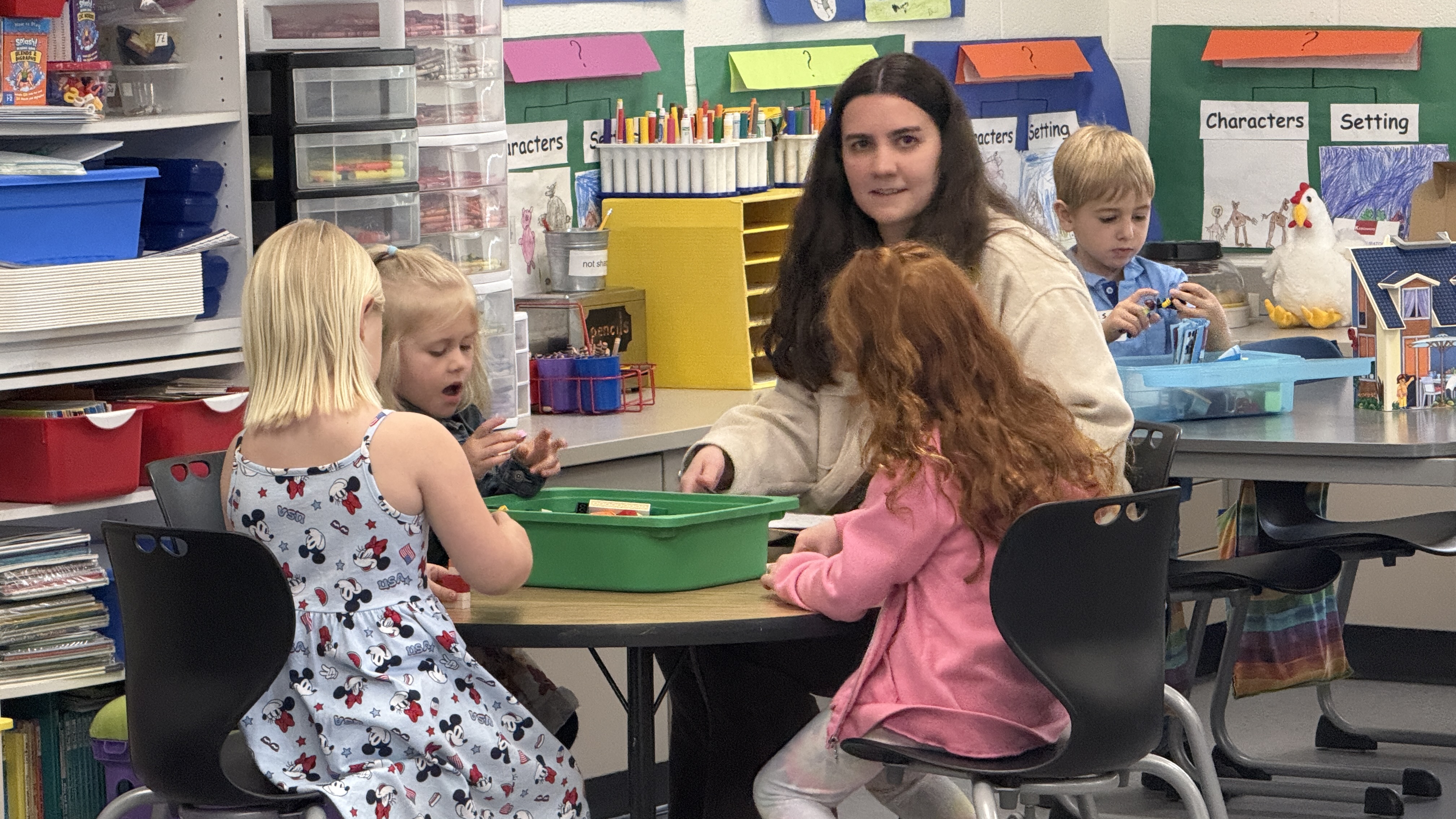 Teacher sitting at table with young students working on a project