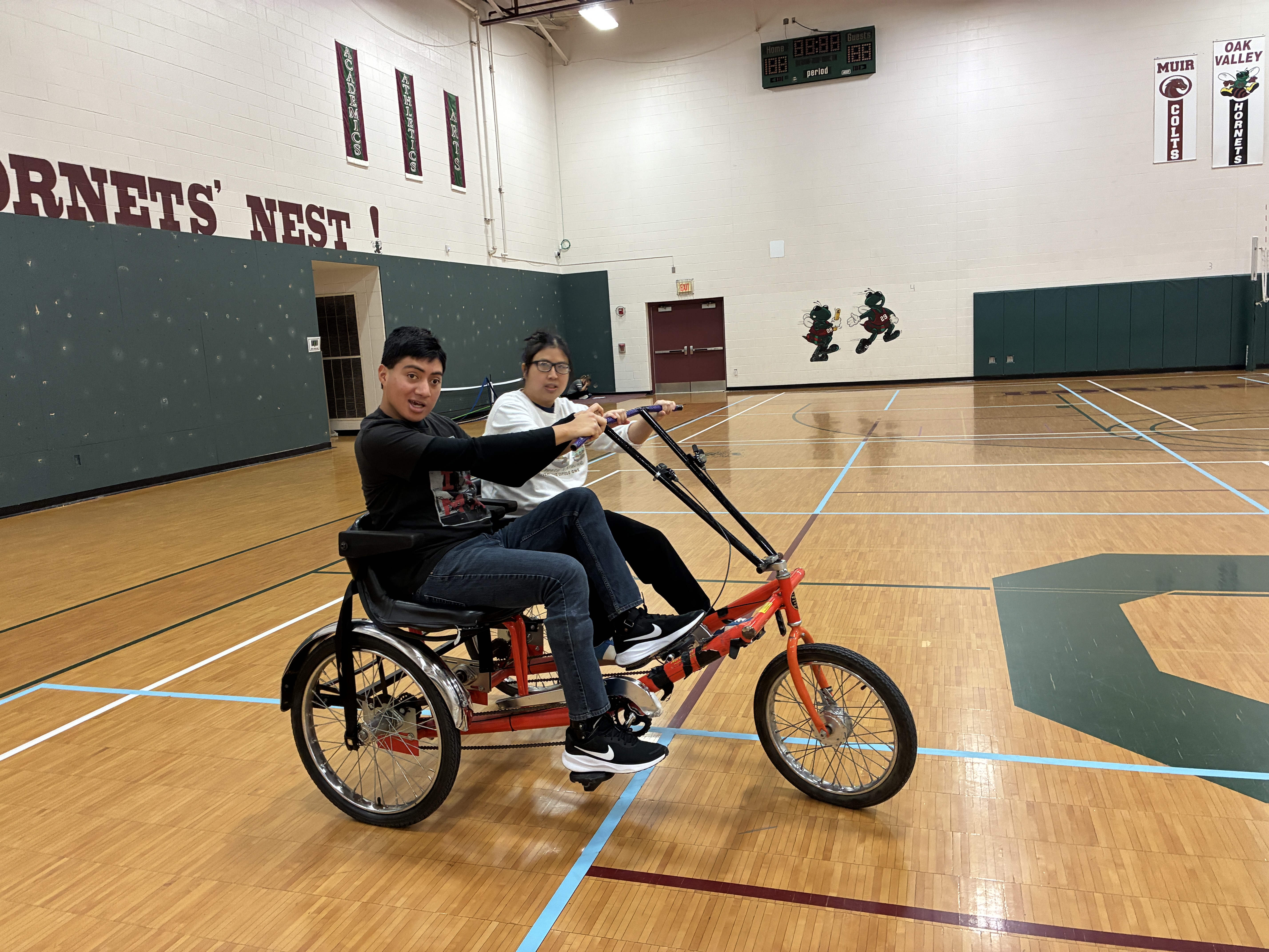 Two students ride bike in gym