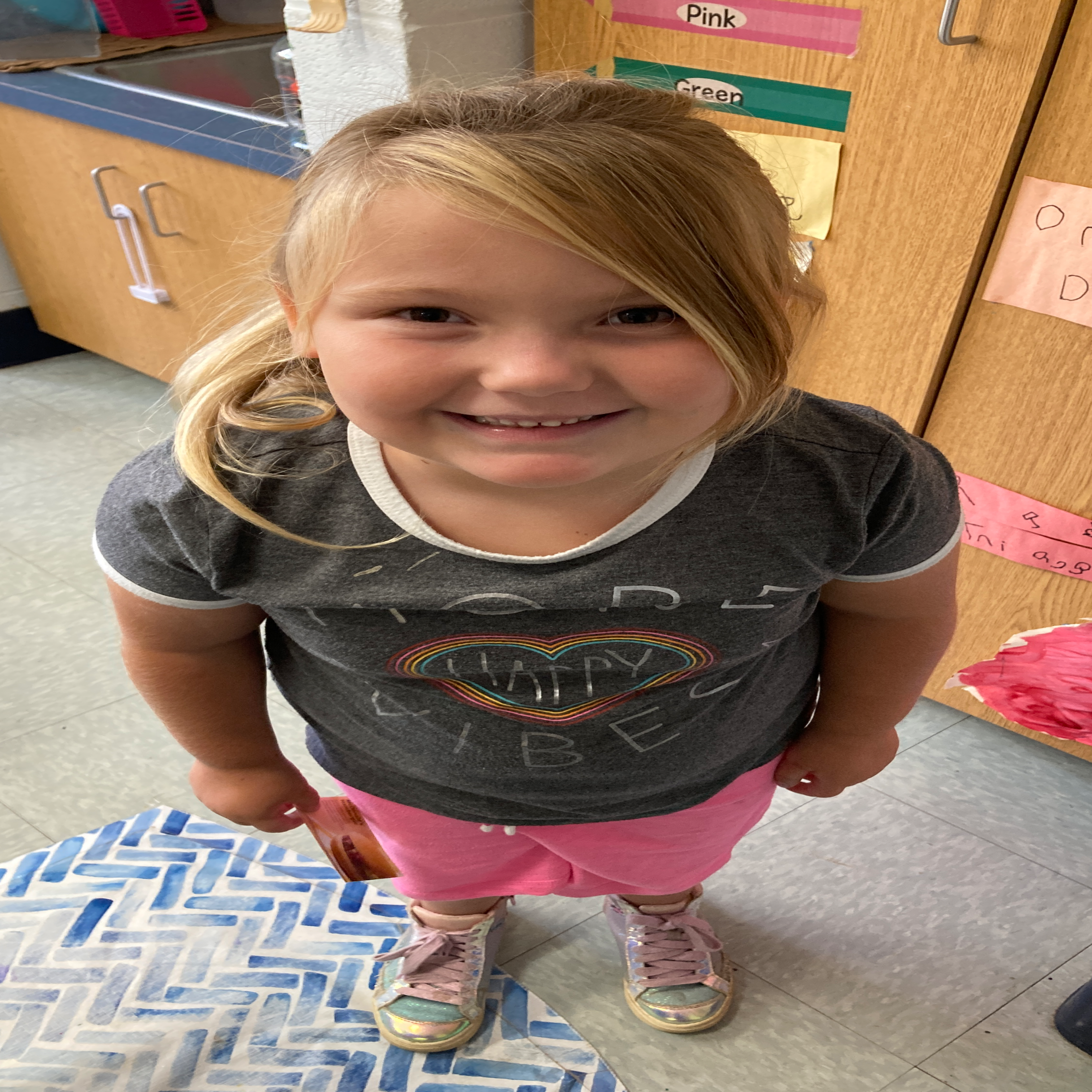 grinning girl with very blonde hair wearing a rainbow heart shirt