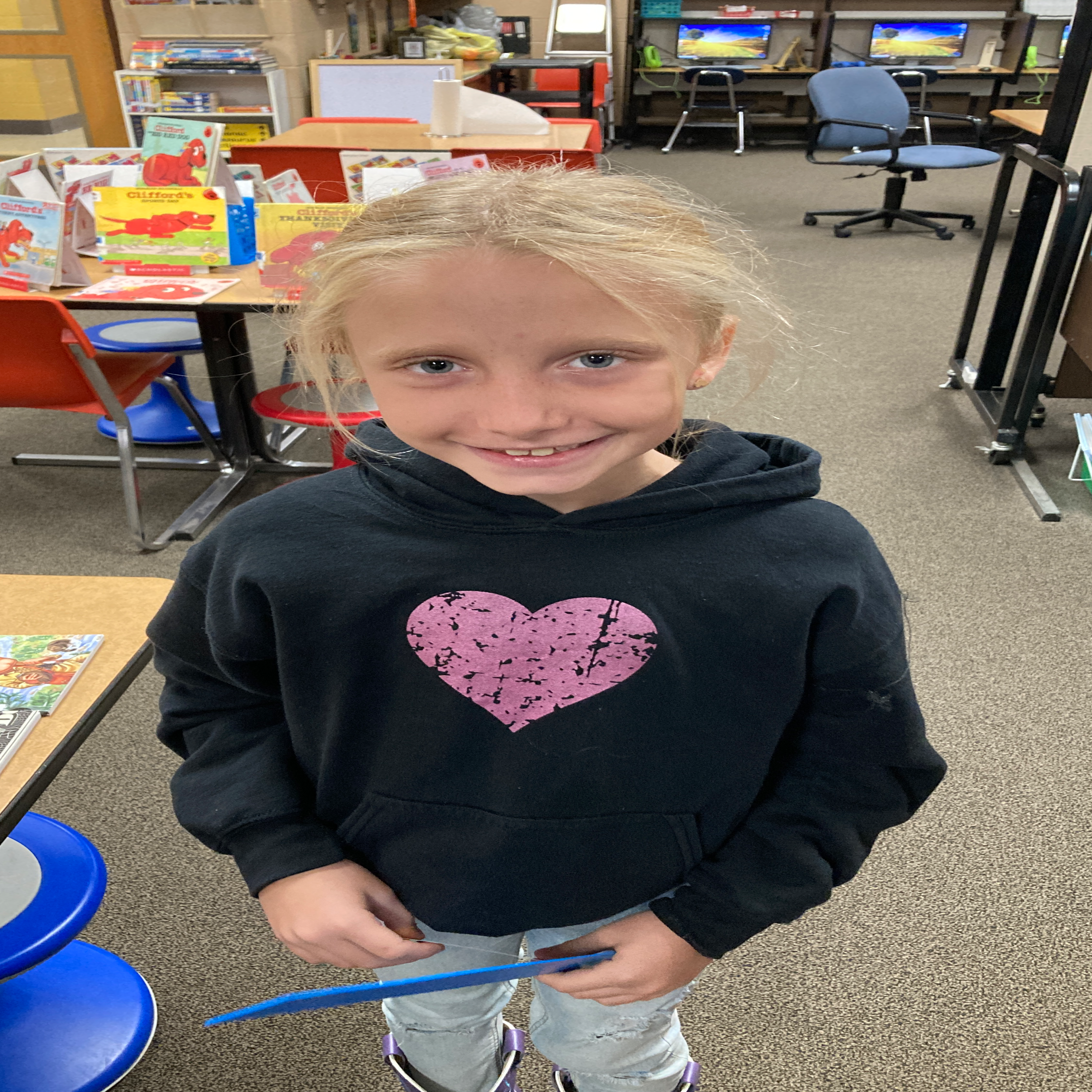 smiling girl with blonde hair in a navy sweatshirt with a pink heart